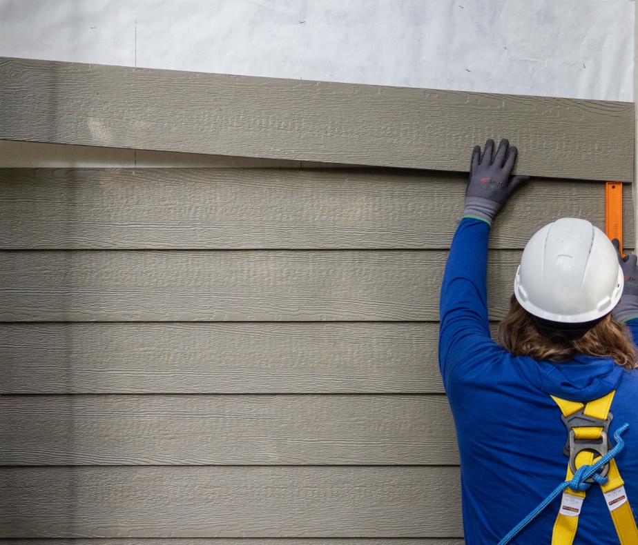 A worker in a hard hat lifting up a sheet of siding to attach to a wall.