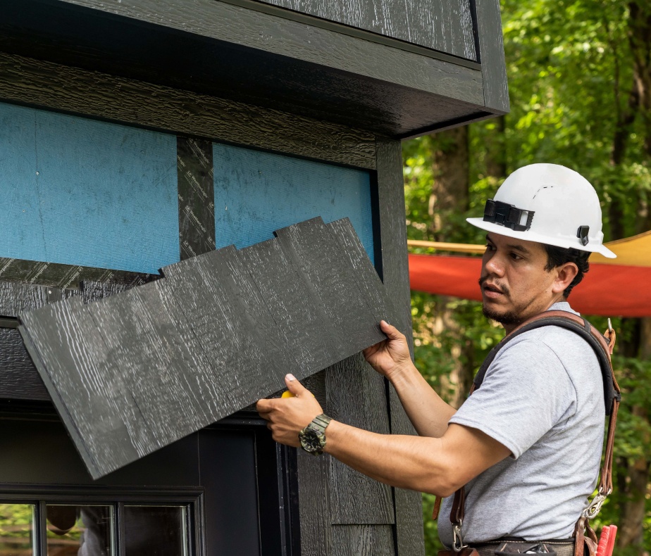 A worker in a hard hat holding a wide piece of siding.