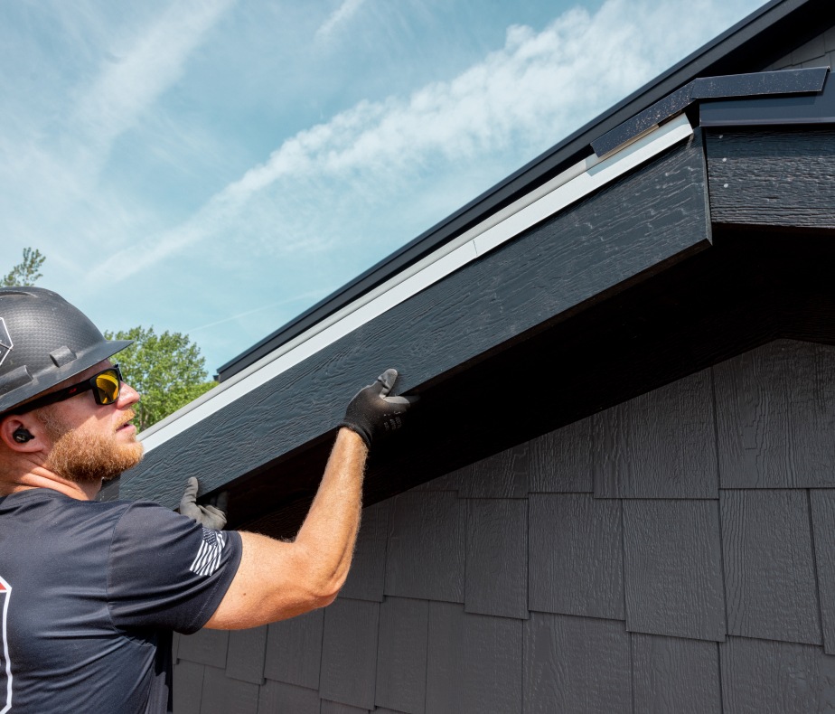 Un travailleur portant un casque de sécurité appliquant une bordure de toit sur l’avant d’une gouttière de toit.