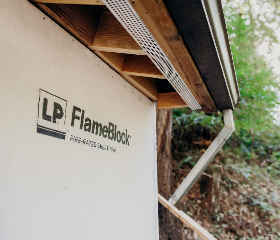 Vue rapprochée du côté extérieur d’une maison, sous un surplomb de toit, avec une feuille de LP Flameblock attachée.