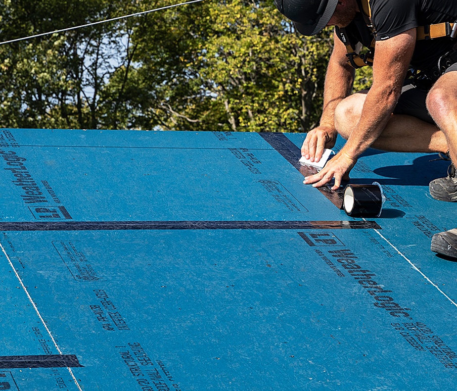 Un trabajador en un techo pegando uniones entre láminas WeatherLogic.