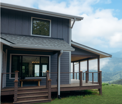 A home with blue siding and a wraparound covered porch in a beautiful countryside landscape.